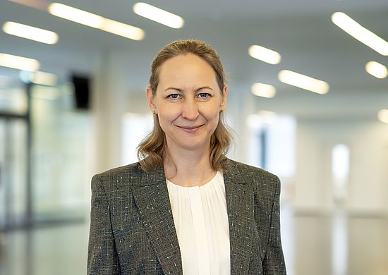 Porträt, lächelnde Frau, dunkeblondes Haar, in einem grauen Blazer und weißer Bluse.