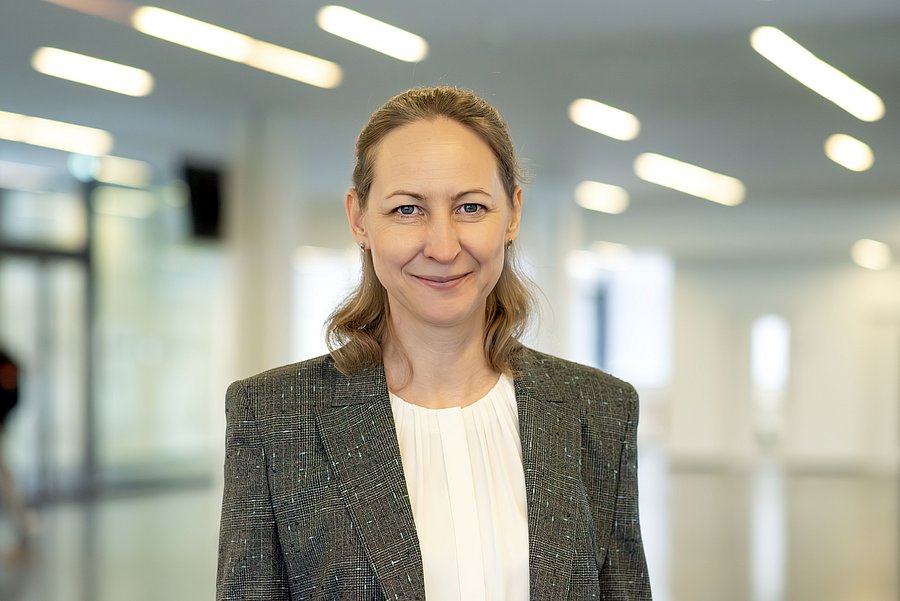 Porträt, lächelnde Frau, dunkeblondes Haar, in einem grauen Blazer und weißer Bluse.