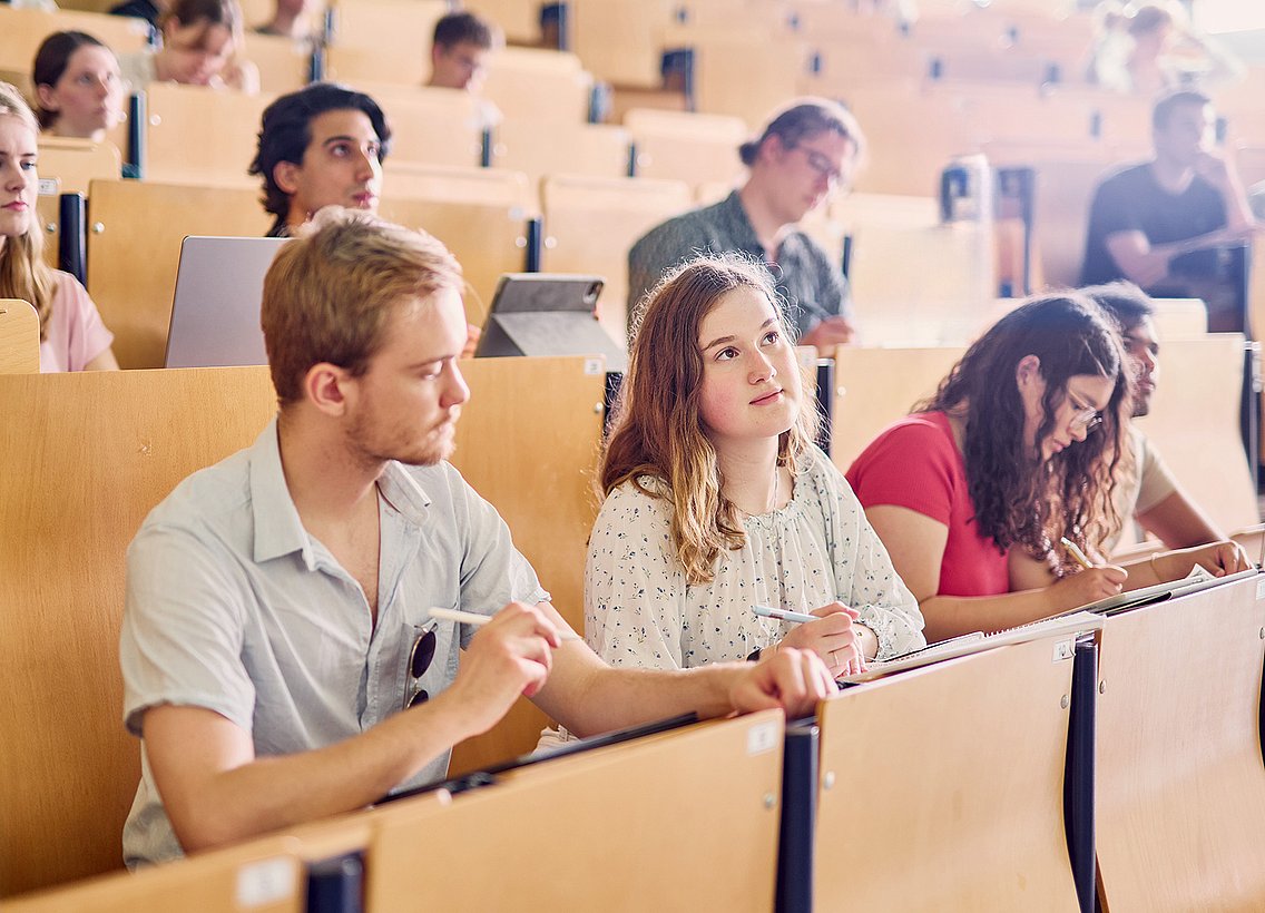 Studierende im Hörsaal, in Tischreihen sitzend, Blick nach Vorne