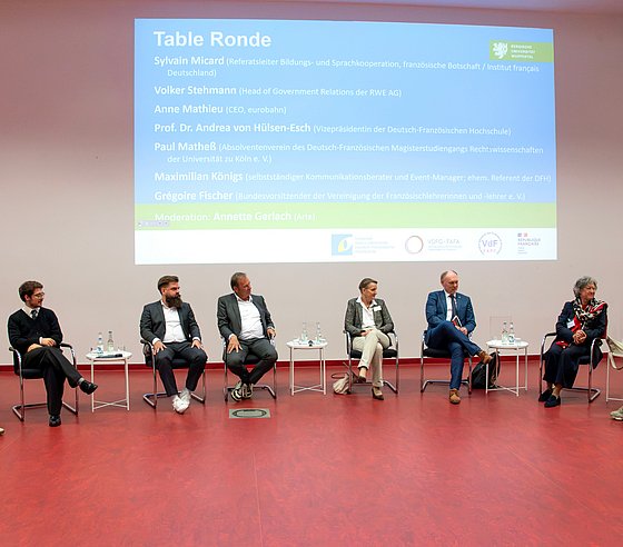 Der Table Ronde: Eine Gruppe von acht Menschen, die vorne im Hörsaal sitzen und der sprechenden Frau ganz rechts zuhören.