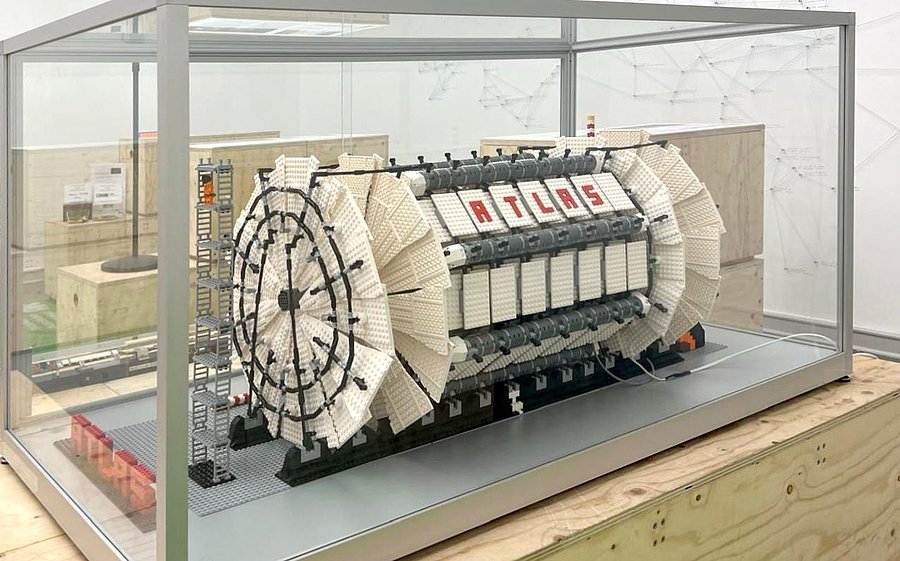 A Lego model of the ATLAS detector, made up of more than 9,500 Lego bricks, is displayed in a glass showcase resting on a wooden plinth. 