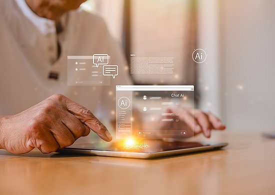 Eine ältere Person nutzt ein Tablet. Über dem Gerät sind grafische Symbole und ein Chatfenster mit dem Hinweis „Chat AI“ eingeblendet, die den Einsatz von Künstlicher Intelligenz veranschaulichen.