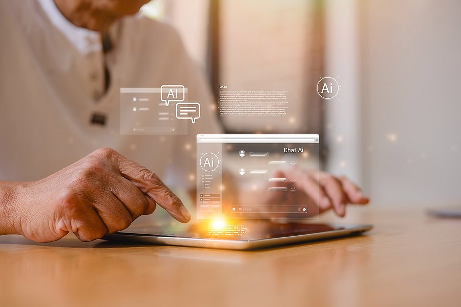 Eine ältere Person nutzt ein Tablet. Über dem Gerät sind grafische Symbole und ein Chatfenster mit dem Hinweis „Chat AI“ eingeblendet, die den Einsatz von Künstlicher Intelligenz veranschaulichen.