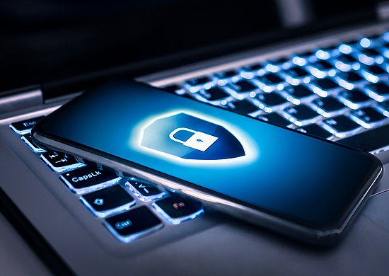Smartphone liegt auf Laptop, der Smartphonebildschirm zeigt ein Schutzschild mit einem Schloss