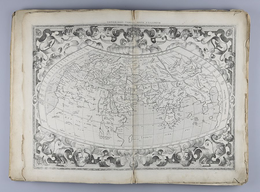 Das Bild zeigt das aufgeschlagene Mercator-Kartenwerk von 1578. Über beide Seiten ist eine Weltkarte in grau-weißer Farbe abgebildet mit verzierenden Illustrationen drum herum. An den Rändern der Seiten sind Papierschäden wie kleine Einrisse erkennbar.