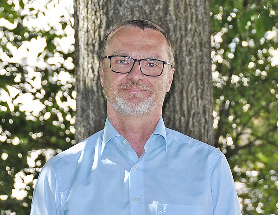 Porträtfoto des Gesundheitsökonomen Prof. Dr. Hendrik Jürges. Er steht vor einem Baum. Er trägt ein hellblaues Hemd.