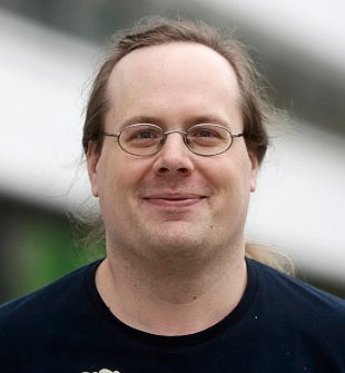 Porträt von Dr. Nico Meuter, hell braune Haare im Zopf, silberne Brille und dunkles T-Shirt, lächelt