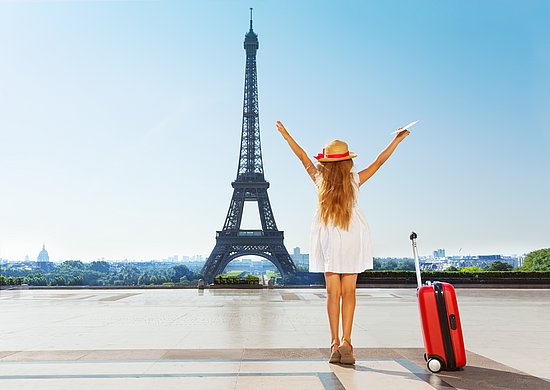 Frau mit Koffer vor dem Eiffelturm in Paris