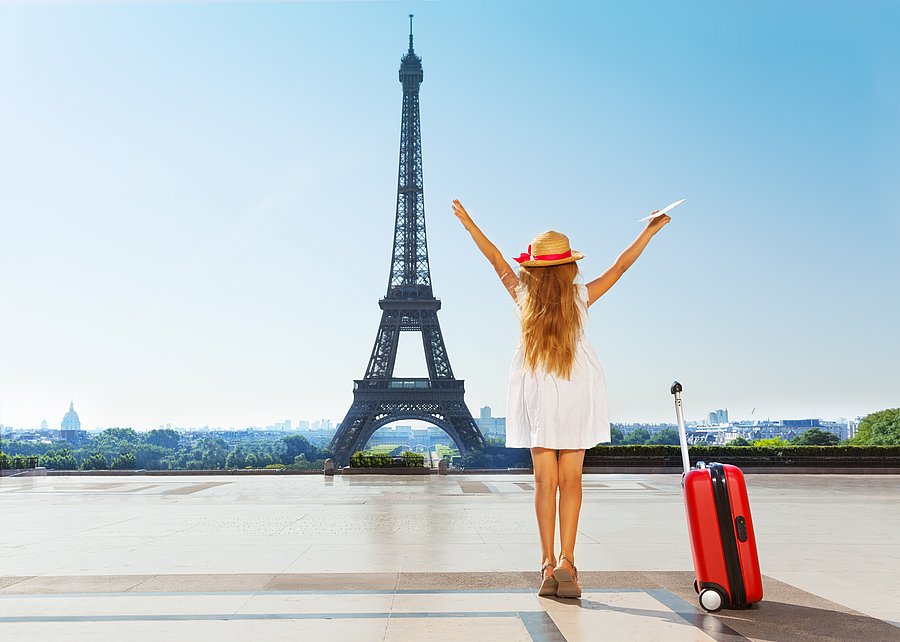 Frau mit Koffer vor dem Eiffelturm in Paris