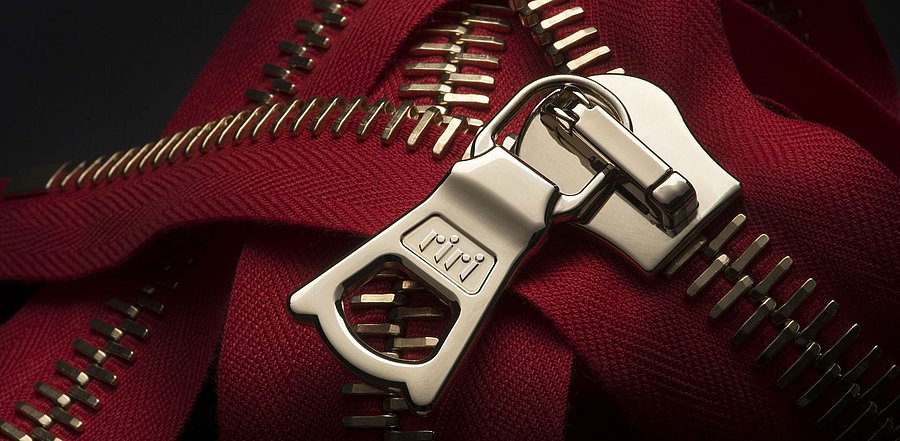 Das Foto zeigt einen rot-silbernen Reißverschluss mit dem charakteristischen Riri-Zipper