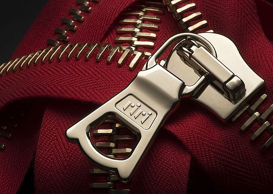 Das Foto zeigt einen rot-silbernen Reißverschluss mit dem charakteristischen Riri-Zipper
