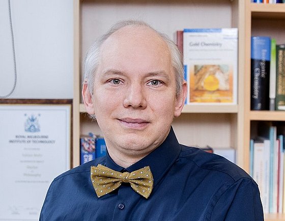 Porträtaufnahme von Prof. Dr. Fabian Mohr. Mann mittleren Alters, graues, kurzes Haar, der obere Teil des Kopfes ist kahl. Er blickt leicht lächelnd in die Kamera, trägt ein dunkelblaues kurzärmliges Hemd und eine dunkelgelbe Fliege. Im Hintergrund stehen mit Büchern gefüllte Regale.