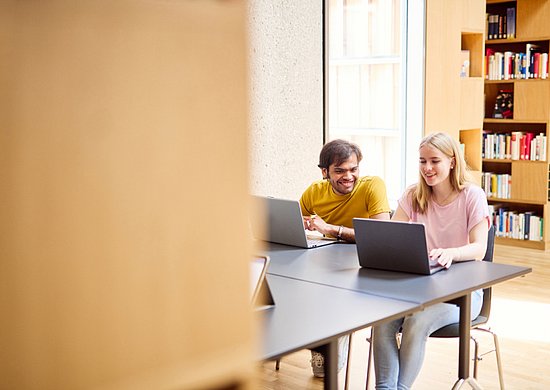 zwei Studierende sitzen in der Bibliothek der Bergischen Universität Wuppertal und arbeiten an einem Laptop