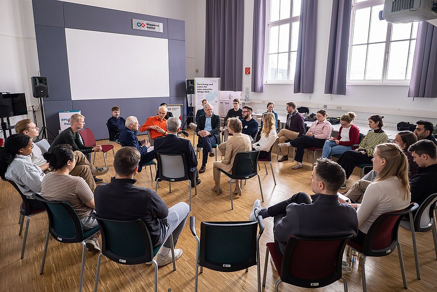 Das Bild zeigt einen Seminarraum. Sieben Menschen sitzen in einem Stuhlkreis und werden von einem größeren Stuhlkreis umrandet.